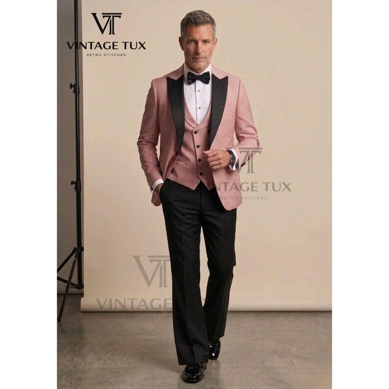 May include: A three-piece suit in a dusty rose color with black lapels and trousers. The suit includes a jacket, vest, and pants. A black bow tie and white dress shirt complete the formal ensemble. The brand name "VINTAGE TUX" is visible.