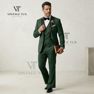 May include: A three-piece dark green suit with a black satin lapel, bow tie, and a white pocket square. The suit is worn with a white dress shirt and black dress shoes. The logo "VINTAGE TUX" is visible.