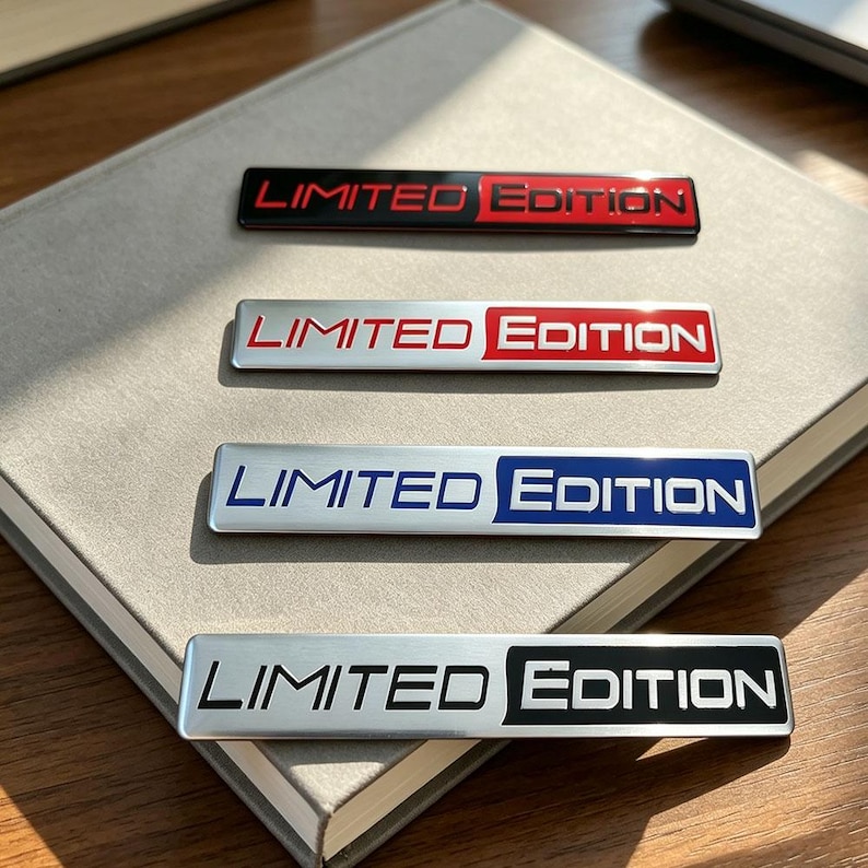 May include: Four rectangular metal badges with the text "LIMITED EDITION" in various color schemes. The badges are black with red text, silver with red text, silver with blue text, and silver with black text. The badges are displayed on a light gray surface.