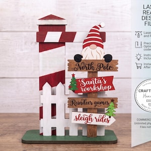 May include: A wooden signpost decoration featuring a red and white striped post, a white picket fence, and a gnome wearing a red and white hat. The signpost includes four directional signs labelled North Pole, Santa's workshop, Reindeer games, and sleigh rides.