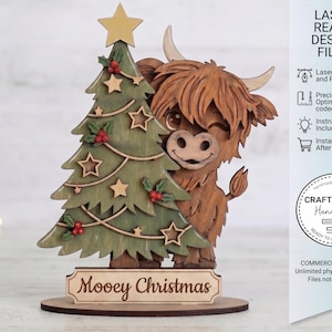 May include: A layered wooden cutout featuring a brown Highland cow peeking from behind a green Christmas tree decorated with stars and red berries. The base includes the text Mooey Christmas. The right side displays text: LASER READY DESIGN FILES.