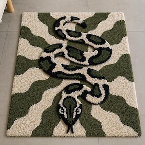 May include: A rectangular rug featuring a snake design in green, cream, and black. The snake is coiled across the rug, set against a wavy background of green and cream. The snake has black spots and a black head.