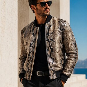 Può includere: Giacca bomber con motivo a pelle di serpente beige e nero, con colletto e polsini neri. La giacca ha una chiusura con cerniera e viene indossata con una maglietta nera e pantaloni neri. La persona indossa occhiali da sole neri.
