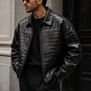 May include: A black, textured leather jacket with a crocodile pattern. The jacket has a collared neckline, a zipper closure, and a relaxed fit. The model is wearing black sunglasses and black pants.