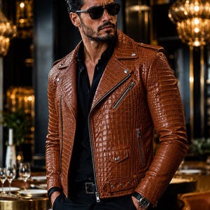 May include: A tan leather motorcycle jacket with a textured crocodile skin pattern, featuring silver-toned metal zips, a notched lapel, a small snap-button pocket, and an adjustable waist belt with a buckle, worn over a black button-down shirt.