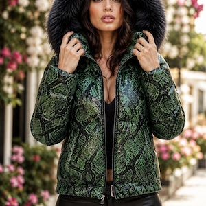 May include: A green and black snakeskin print puffer jacket featuring a full-length front zipper closure and a large, plush black faux fur-trimmed hood. The jacket has a quilted construction and long sleeves, providing a textured appearance.