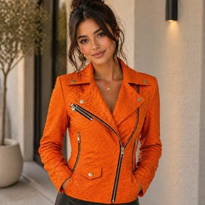 May include: Bright orange leather jacket with a snakeskin texture, diagonal zip, and black zippers. The jacket has a classic biker style with a notched collar and button details. The jacket is a vibrant fashion statement.