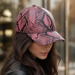 May include: A baseball cap featuring a vibrant pink and black snakeskin pattern. The cap has a structured crown and a curved brim, with a textured surface that mimics the appearance of reptile scales across the entire exterior fabric.