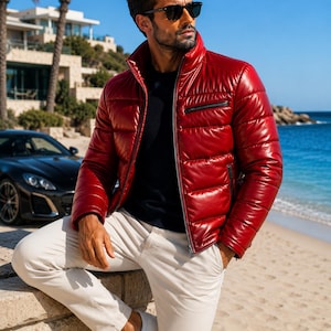 Könnte beinhalten: Eine glänzende rote Steppjacke mit hohem Kragen, Frontreißverschluss und horizontalen Steppnähten. Die Jacke verfügt über eine Reißverschlusstasche auf der Brust sowie zwei Seitentaschen und wird über einem dunkelblauen Pullover zu beigen Hosen getragen.
