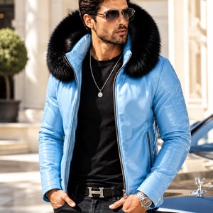 May include: A bright blue leather jacket featuring a large black faux fur hood trim, a silver front zipper, and long sleeves. The jacket is worn over a plain black t-shirt, paired with black jeans, a black belt with a silver H buckle, and a silver necklace.
