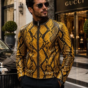 May include: A long-sleeve jacket featuring a vibrant yellow and black snakeskin pattern, a high collar, and a central silver-toned zipper closure. The garment is worn with plain black trousers and includes zippered side pockets on the front.