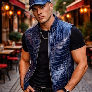 Puede incluir: Un chaleco de cuero azul marino con un patrón de cocodrilo, combinado con una gorra de béisbol a juego. El chaleco tiene una cremallera frontal y una camiseta negra debajo. Una cadena de oro y un reloj negro completan el look.