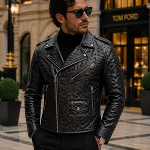 Könnte beinhalten: Schwarze Leder-Motorradjacke mit strukturiertem Muster, Reverskragen, asymmetrischem Reißverschluss und mehreren Taschen. Die Jacke wird über einem schwarzen Rollkragenpullover getragen. Die Person trägt eine Sonnenbrille und eine Uhr.