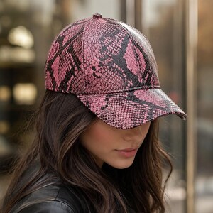 May include: A baseball cap featuring a vibrant pink and black snakeskin pattern. The cap has a structured crown and a curved brim, with a textured surface that mimics the appearance of reptile scales across the entire exterior fabric.