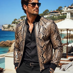 May include: A bomber jacket featuring a metallic gold and black snakeskin pattern with a black ribbed collar, cuffs, and hem. The jacket is worn over a black button-down shirt and black trousers with a black belt and a gold-toned wristwatch.