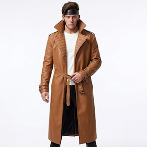 May include: A long, brown leather trench coat with a belt, large lapels, and decorative stitching on the shoulders. The coat has long sleeves with buckle details at the cuffs. The coat is worn over a white shirt and black pants.
