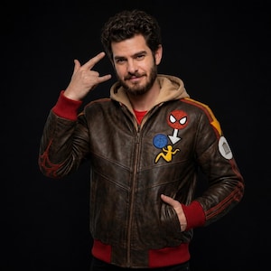 May include: A brown leather bomber jacket with a beige hood, red ribbed cuffs and hem, and a red inner lining. The jacket features embroidered patches on the chest, including a Spider-Man mask, a blue web, and a yellow figure, plus a white circular patch.