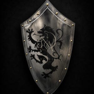 May include: A heater shield made of polished dark metal featuring a prominent black silhouette of a rampant lion. The shield is bordered by a raised rim secured with evenly spaced gold-colored rivets along the edges and a pointed top section.
