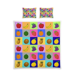 May include: A bedding set consisting of a large rectangular comforter and two square pillow shams. The fabric features a repeating grid pattern of colorful squares, each containing a different fruit illustration including apples, bananas, grapes, and pineapples.
