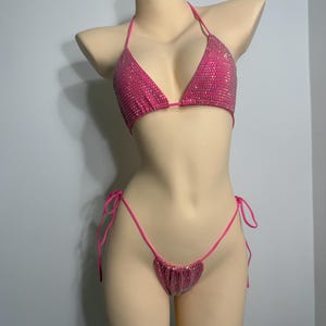 Op de afbeelding: Een felroze bikiniset met sprankelende versieringen. De driehoekige top en de string-bikini-broek worden op een mannequin getoond. De bikini heeft een levendige roze tint, perfect voor badkleding.