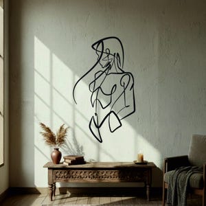Peut inclure: Une œuvre d'art murale en métal noir représentant un dessin au trait minimaliste d'une personne. L'œuvre est fixée sur un mur de couleur claire. La pièce comprend également un banc en bois, un vase avec des plantes séchées et une bougie.