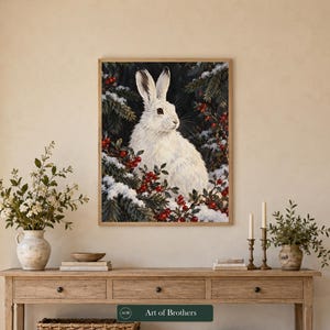 May include: A rectangular wall art print featuring a white rabbit sitting amidst snow-covered evergreen branches and bright red berries. The artwork is framed in a light wood frame and displays the text Art of Brothers at the bottom.