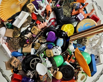 May include: A glass bowl filled with a variety of colorful trinkets, toys, and game pieces.  There are small plastic animals, dice, letter tiles, seashells, and other miscellaneous items.