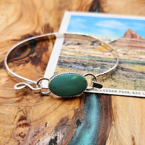 May include: A silver bangle bracelet with a turquoise stone set in a silver oval. The bracelet is open and has a simple design.