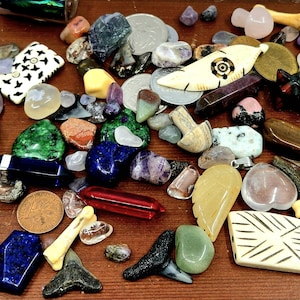 May include: A selection of gemstones, crystals, and decorative items in diverse shapes and colours. Includes polished stones, bone carvings, and small glass bottles. The items are arranged on a wooden surface, creating a colourful display.