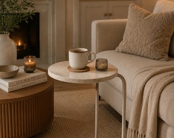 May include: A round side table with two tiers featuring a light beige stone-look surface and a curved metal frame. The table has a circular top and a matching circular base connected by a single vertical support, providing a compact design.