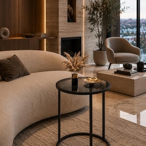 May include: A round side table with a black metal frame and a dark glass top. The table features a slender cylindrical base and a circular tabletop, holding a small vase with dried pampas grass and a shallow gold-toned decorative bowl.