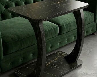 May include: A black marble-topped side table with gold veining. The table has a rectangular top and a curved, arch-shaped base. The table is set in front of a green tufted sofa, creating a luxurious aesthetic.