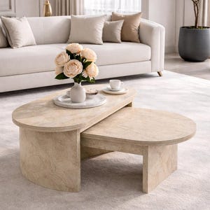 Peut inclure: Un ensemble de tables basses en pierre de couleur claire, compos&eacute; de deux pi&egrave;ces. La table sup&eacute;rieure est ovale et chevauche une table plus petite, rectangulaire. Un vase de fleurs et une tasse et une soucoupe sont pos&eacute;s sur la table sup&eacute;rieure.