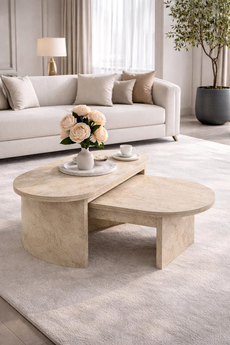 Peut inclure: Un ensemble de tables basses en pierre de couleur claire, compos&eacute; de deux pi&egrave;ces. La table sup&eacute;rieure est ovale et chevauche une table plus petite, rectangulaire. Un vase de fleurs et une tasse et une soucoupe sont pos&eacute;s sur la table sup&eacute;rieure.