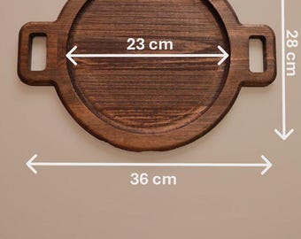 May include: A round dark brown wooden serving tray with two side handles. The tray features a 23 cm inner diameter, a 28 cm total height, and a 36 cm total width including the handles, as indicated by the white measurement arrows.