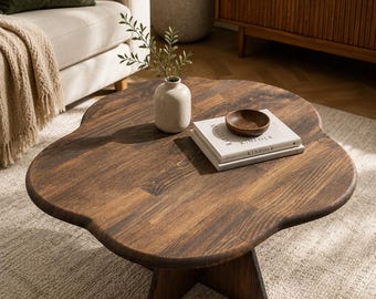 May include: A dark brown wooden coffee table with a distinct flower-shaped top and a sturdy cross-base support. The surface features a visible wood grain pattern and smooth, rounded edges, providing a stable platform for decorative items.