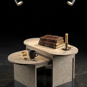 Peut inclure: Une table basse en pierre grise clair &agrave; deux niveaux avec une pile de livres, des lunettes, une bougie et une tasse &agrave; caf&eacute;. La table est &eacute;clair&eacute;e par deux spots noirs.
