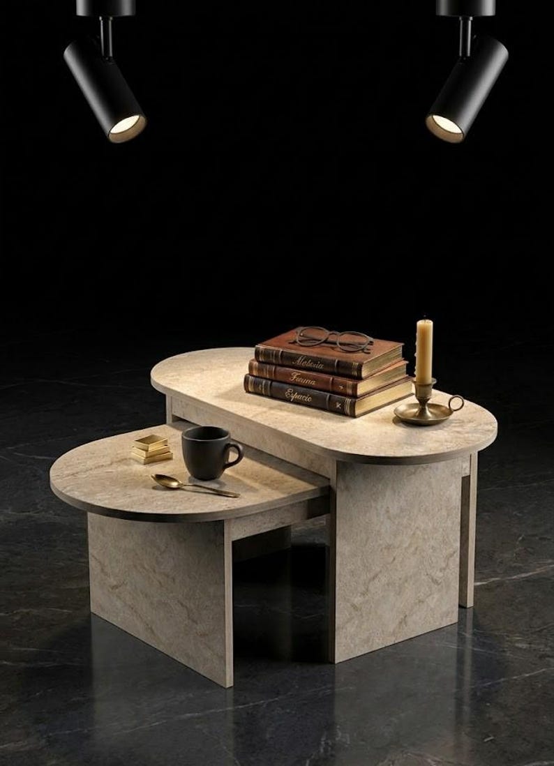 Peut inclure: Une table basse en pierre grise clair &agrave; deux niveaux avec une pile de livres, des lunettes, une bougie et une tasse &agrave; caf&eacute;. La table est &eacute;clair&eacute;e par deux spots noirs.