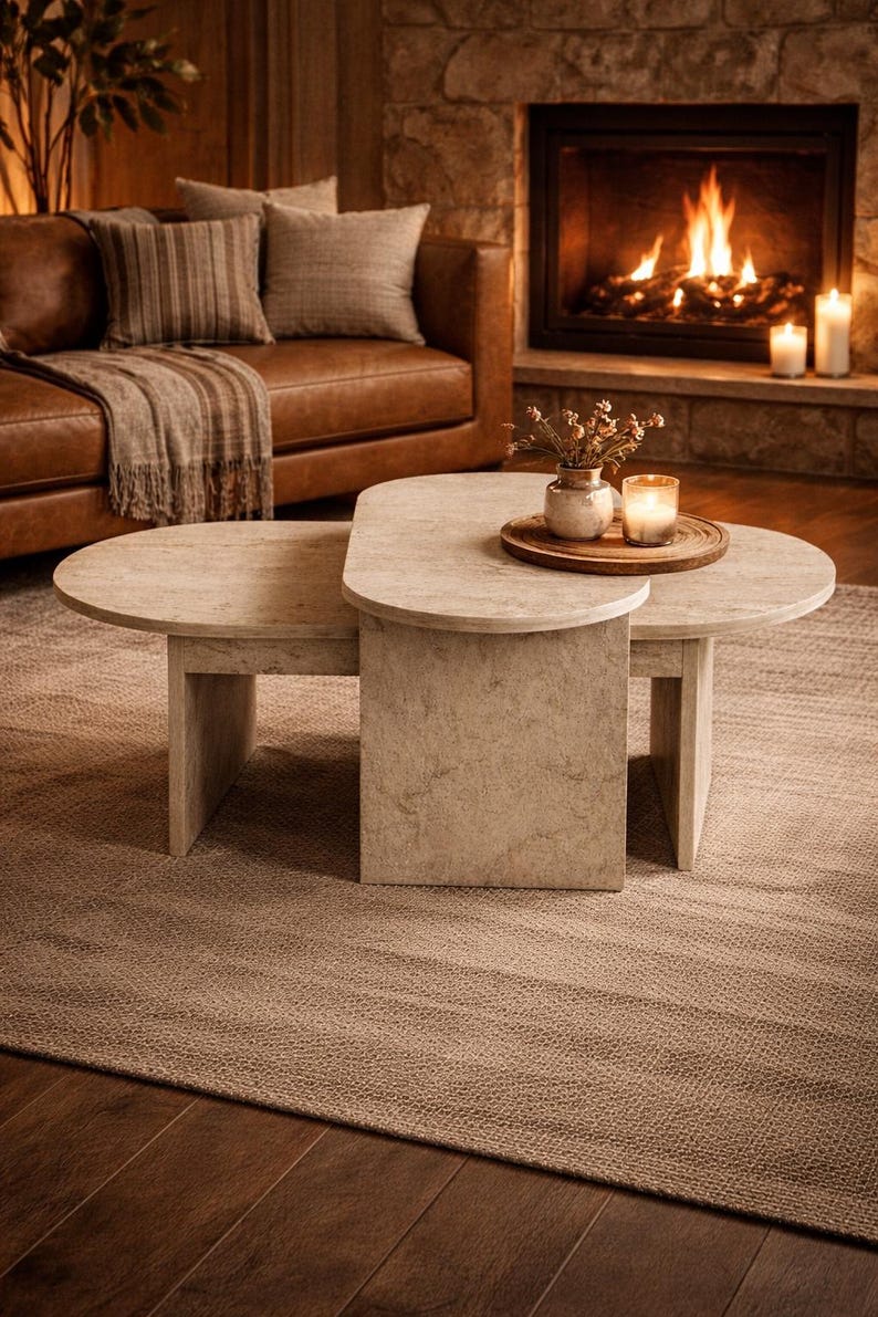 Peut inclure: Une table basse beige clair en deux parties avec un design imbriqu&eacute; unique. La table pr&eacute;sente une texture naturelle semblable &agrave; de la pierre et repose sur un tapis aux tons neutres. Un canap&eacute; en cuir et une chemin&eacute;e sont en arri&egrave;re-plan.