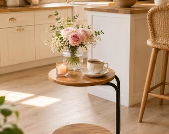 May include: A round two-tier side table with a dark wood finish and a black metal frame. The table features two circular shelves and is supported by a curved metal structure with small wheels at the base for mobility, providing a compact surface.