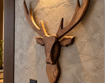May include: A wall-mounted deer head sculpture crafted from polished brown wood with prominent antlers. The piece features a smooth, faceted design and is positioned directly beneath a small, black, rectangular wall light fixture.