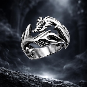 Peut inclure: Bague argentée représentant un dragon. Le design détaillé du dragon entoure l'anneau. L'arrière-plan sombre met en valeur la brillance métallique et le thème fantastique de la bague.