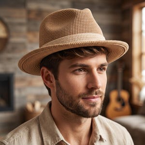 May include: A tan fedora hat with a woven texture and a light-colored band. The hat has a classic shape with a slightly indented crown and a brim that curves downward. The hat is a neutral color and suitable for various outfits.