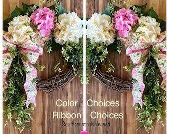 May include: Two grapevine wreaths, each adorned with cream and pink hydrangea blooms, green foliage, and a floral ribbon bow. The text "Color Choices Ribbon Choices SouthernbornNblessed" is visible. A pink heart is at the bottom.
