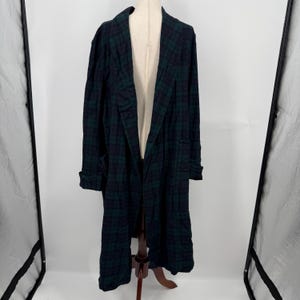 May include: A long-length robe featuring a dark navy blue and forest green plaid tartan pattern. The garment has a wide shawl collar, long sleeves with folded cuffs, and an open front design, displayed on a mannequin for a clear view.