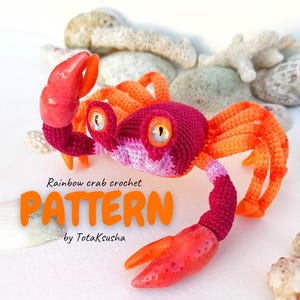 May include: A handmade crochet crab in shades of red, orange, and pink. The crab has large, expressive eyes and is posed on a surface with seashells and coral. The text "Rainbow crab crochet PATTERN" is visible.