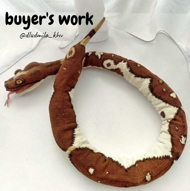 May include: A handmade snake toy in brown, white, and tan. The snake has detailed stitching, a forked pink tongue, and yellow eyes. The text "buyer's work" and the seller's username are visible in the image.