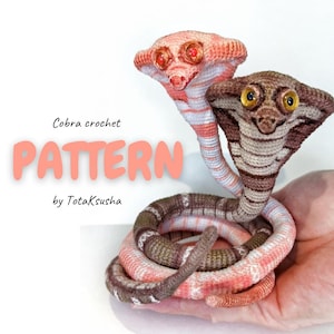 May include: Two crocheted cobra snakes with glossy eyes, one in shades of pink and white, the other in brown and tan. The text reads Cobra crochet PATTERN by Totaksusha. The snakes are coiled together with hoods flared in a display.