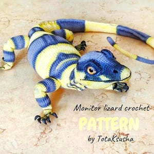 Könnte beinhalten: Gehäkelte Warane in blau-gelben Streifen. Der Echse hat einen detaillierten Kopf mit einem orangefarbenen Auge und schwarzen Krallen. Der Text "Monitor lizard crochet PATTERN by TotakSusha" ist sichtbar.