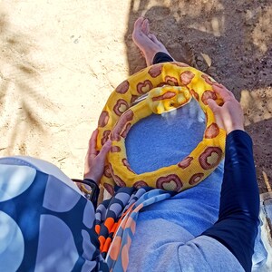 May include: A yellow and brown snake toy is held. The toy is coiled, with brown spots on a yellow background. The person is wearing a blue sweatshirt and a patterned scarf. The image is taken from an overhead perspective.